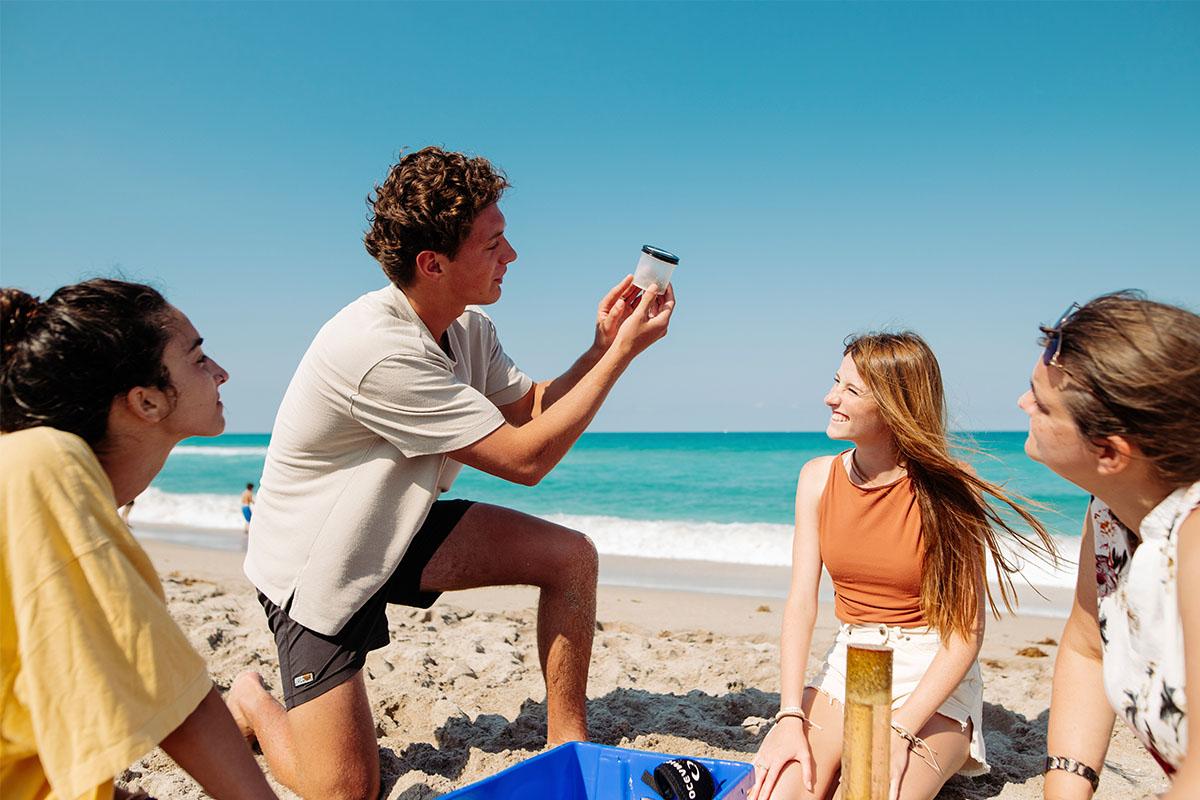 marine biology students at the beach looking at a jar of sand